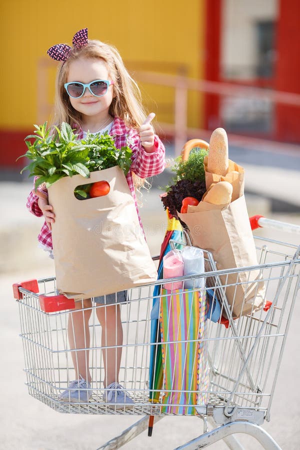 En liten flicka med stor vagn köper färsk mat och färska grönsaker i en stor stormarknad bara under sommaren.