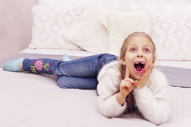 En liten flicka med en vit tröja och blå jeans som ligger på den dåliga och dräktiga arkivbilder En liten flicka med en vit tröja och blå jeans som ligger på den dåliga och dräktiga arkivbilder