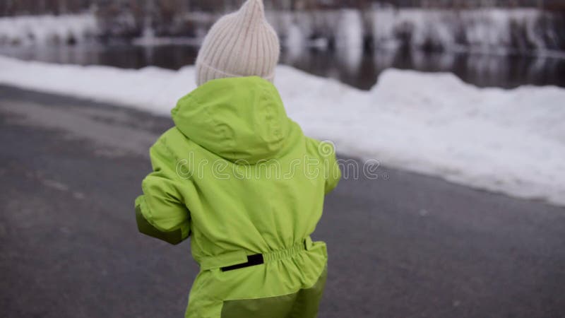 En liten flicka rider en skoter bredvid floden på vintern.