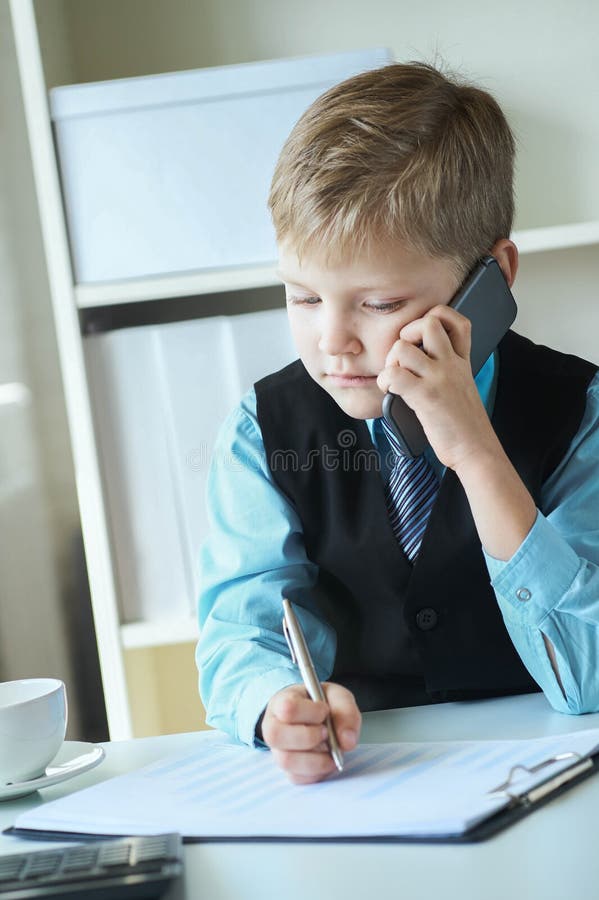 En liten förtroendefull chefschef gör anteckningar och samtal på telefonen som sitter vid skrivbordet med en bärbar dator i royaltyfri fotografi