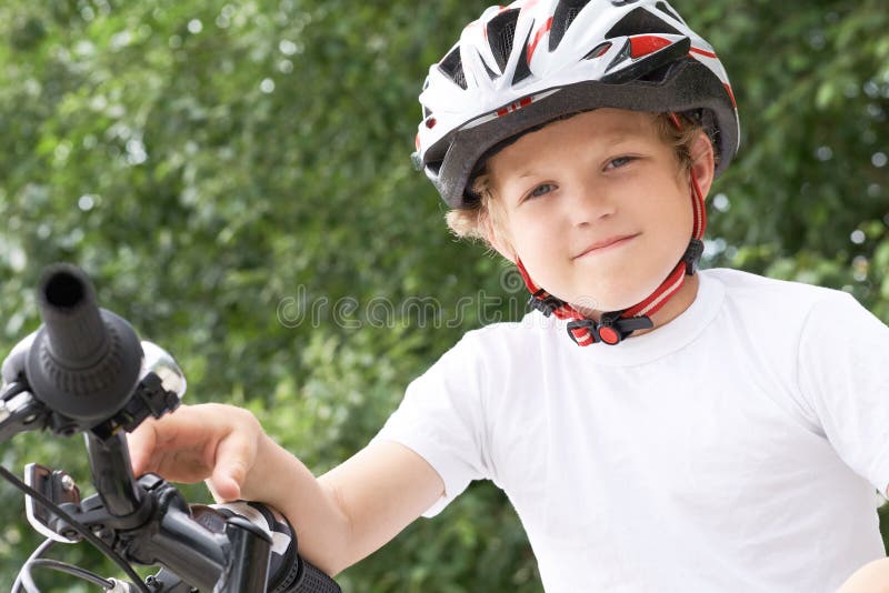 En liten kaukasisk pojke i skyddande hjälm som lutar sig mot kamerans cykel Tonåring redo att åka royaltyfri fotografi