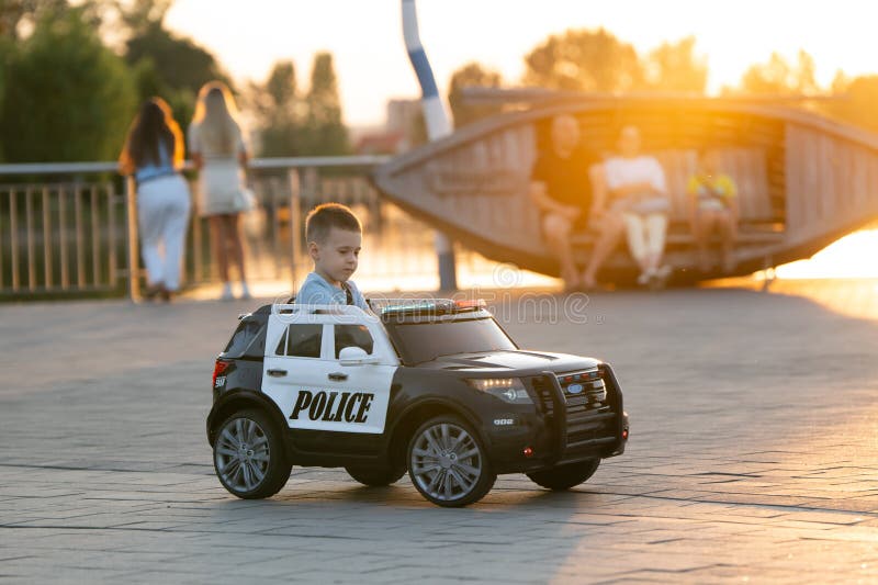En liten kaukasisk småbarnspojke på tre och ett halvt år rider en leksaksbil i en sommarpark nära sjön royaltyfri fotografi