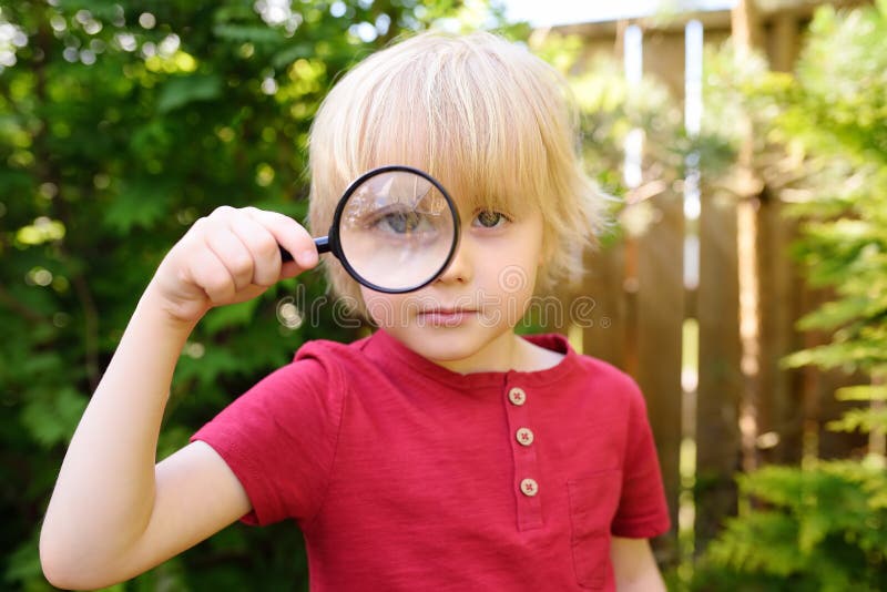 En liten pojke som leker med förstoringsglas Den lilla pojken tittade noga på dig med förstorare arkivbilder En liten pojke som leker med förstoringsglas Den lilla pojken tittade noga på dig med förstorare arkivbilder