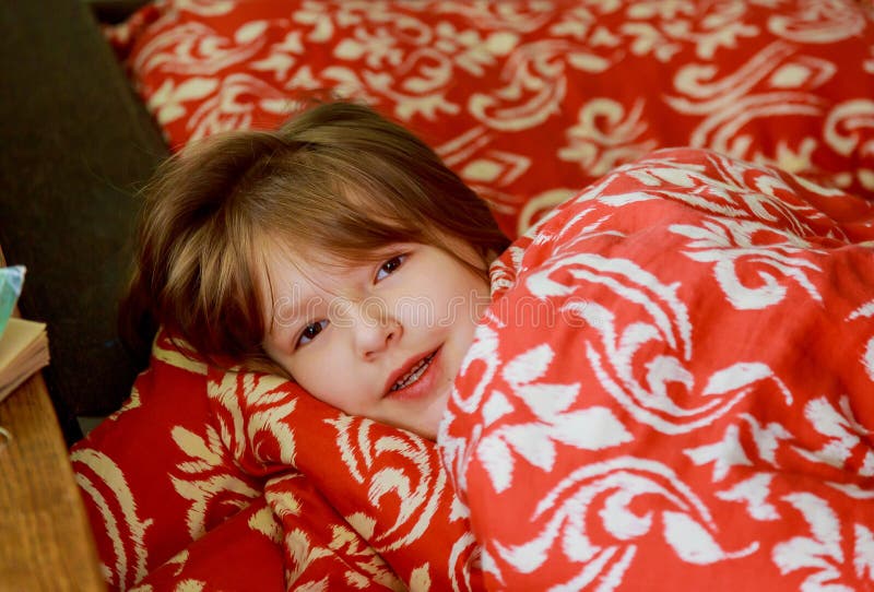 En liten sjuk flicka i sovrummet Liten flickasammanträde på bära för säng pyjamas royaltyfri bild En liten sjuk flicka i sovrummet Liten flickasammanträde på bära för säng pyjamas royaltyfri bild