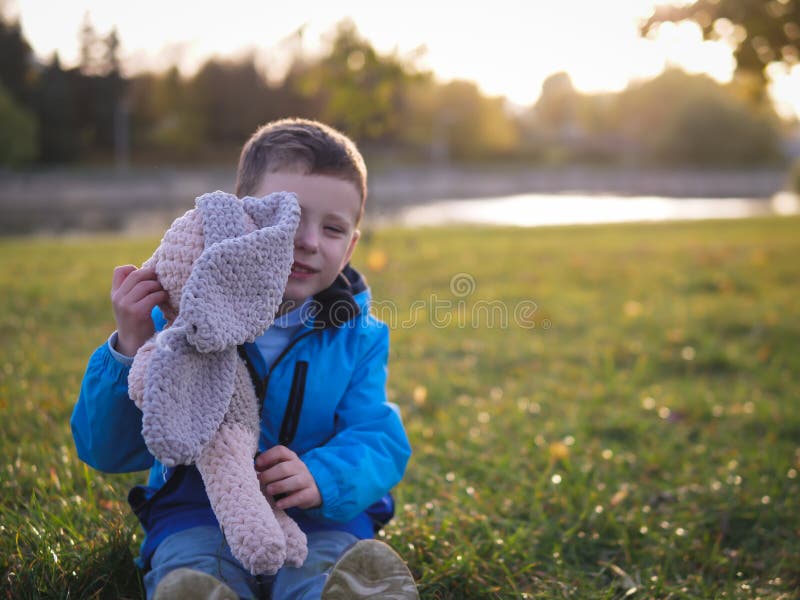 En liten slavisk joyful pojke på den gräta porträtten på våren i en stadspark med en mjuk leksak arkivfoto