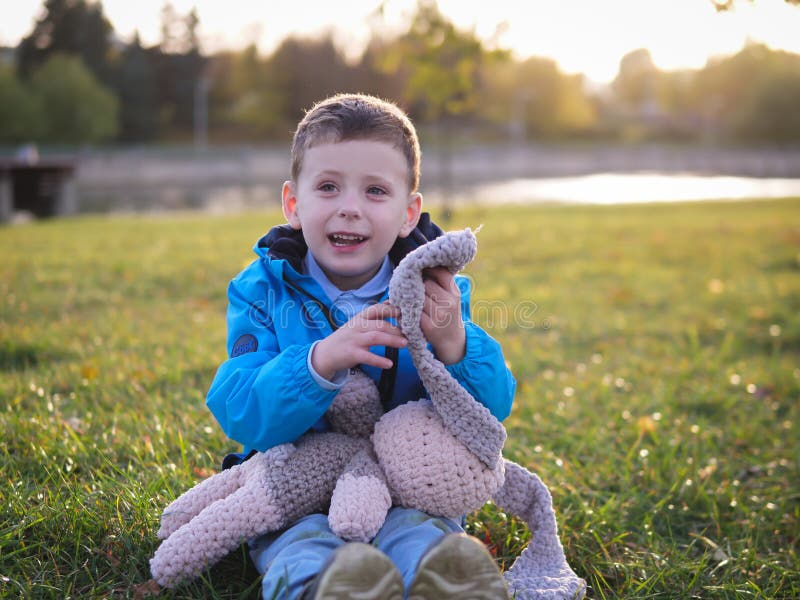 En liten slavisk joyful pojke på den gräta porträtten på våren i en stadspark med en mjuk leksak royaltyfri fotografi