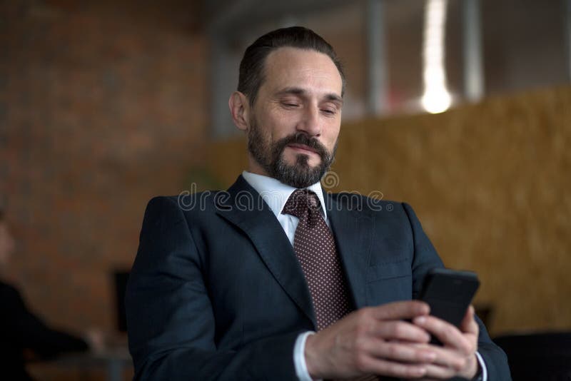 En lyckad affärsman som läser ett textmeddelande på en mobiltelefon, medan sitta i hans kontor royaltyfria bilder En lyckad affärsman som läser ett textmeddelande på en mobiltelefon, medan sitta i hans kontor royaltyfria bilder