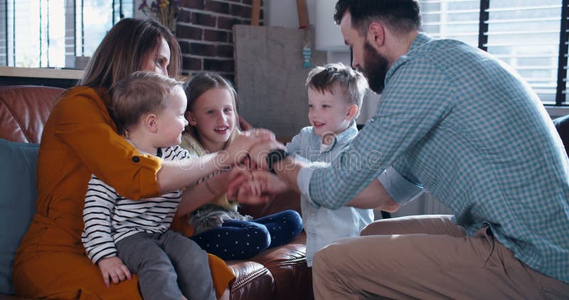 En lycklig ung kaukasisk familj med tre barn går hand i hand och gläds tillsammans åt tiden i hemmet för långsam rörelse.