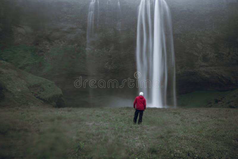En man med röd jacka framför den berömda Seljalandsfoss-vattenfallet på Island i regnet royaltyfri fotografi En man med röd jacka framför den berömda Seljalandsfoss-vattenfallet på Island i regnet royaltyfri fotografi