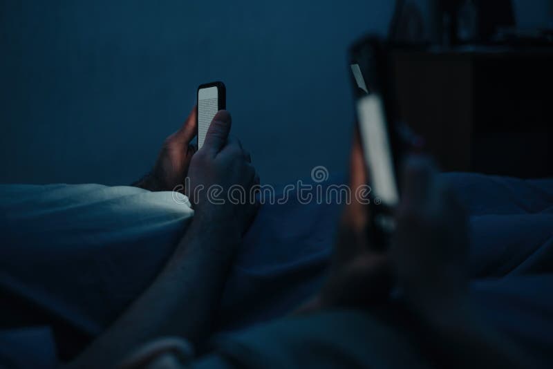 En man och en kvinna ligger i pastellerna på natten och använder sina telefoner. Kontrollera sociala medier före sänggående. arkivfoton En man och en kvinna ligger i pastellerna på natten och använder sina telefoner. Kontrollera sociala medier före sänggående. arkivfoton