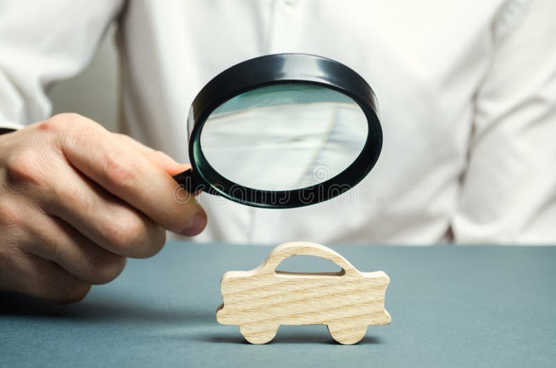 En man rymmer ett förstoringsglas över en miniatyrträbil Den beräknade kostnaden av automatiskn Analys och teknisk kontroll av royaltyfri fotografi En man rymmer ett förstoringsglas över en miniatyrträbil Den beräknade kostnaden av automatiskn Analys och teknisk kontroll av royaltyfri fotografi