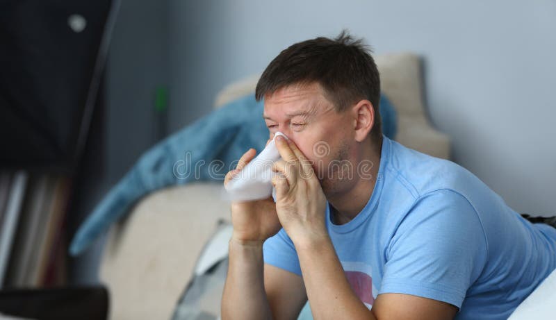 Man blowing his nose in a napkin while sitting at home on sofa portrait. Man blowing his nose in a napkin while sitting at home on sofa portrait