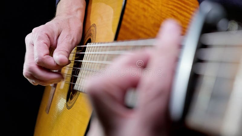 En man som leker på akustisk gitarr på mörk bakgrund nära.