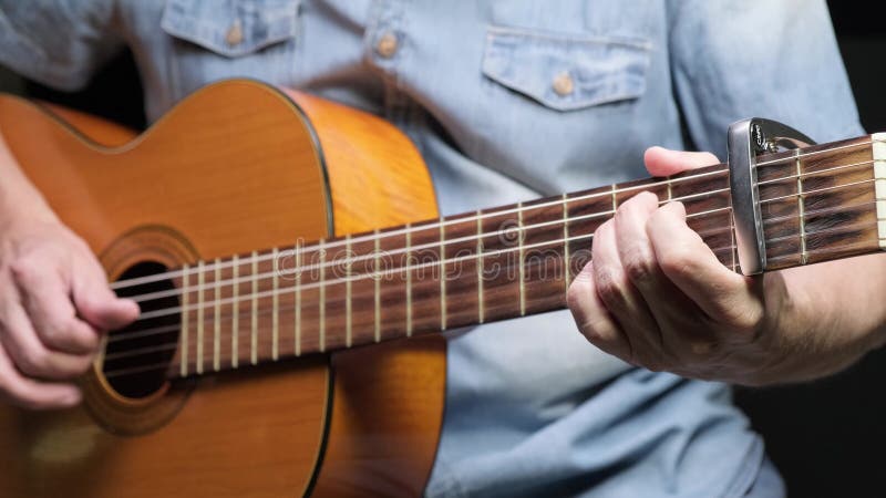 En man som leker på akustiska gitarrer på mörk bakgrund. tama hobbyer