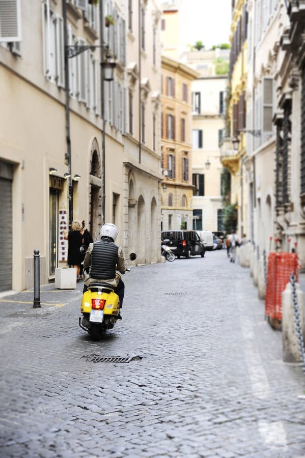 En man som rider en gul vespasparkcykel på en typisk gata av Rome royaltyfri foto En man som rider en gul vespasparkcykel på en typisk gata av Rome royaltyfri foto