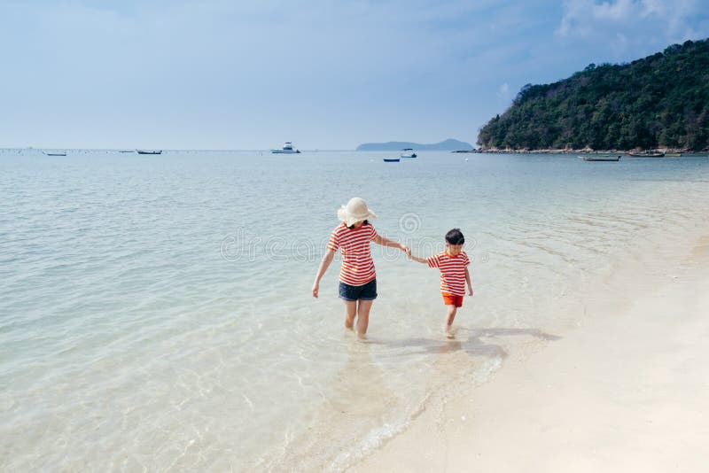 En moder- och soninnehavhand och gå på strand- och havsdet fria på solnedgången arkivfoton En moder- och soninnehavhand och gå på strand- och havsdet fria på solnedgången arkivfoton