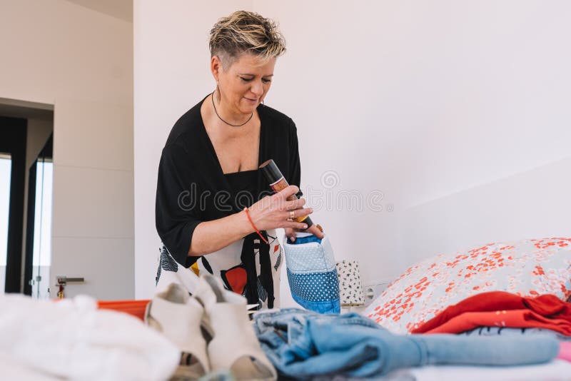 mature woman checking luggage to make sure everything is ready before her summer trip. leisure and holiday concept. room, illuminated by natural light, suitcase with clothes. mature woman checking luggage to make sure everything is ready before her summer trip. leisure and holiday concept. room, illuminated by natural light, suitcase with clothes.