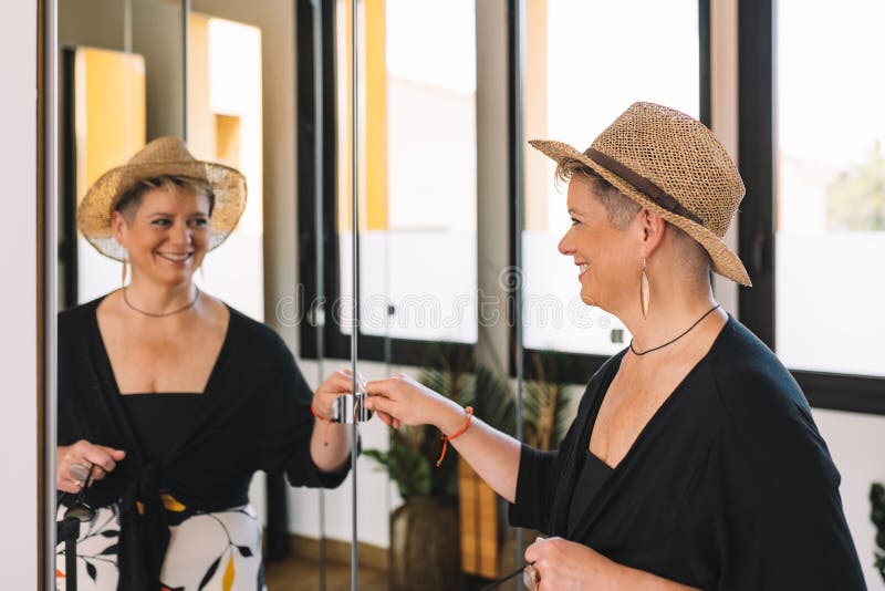 mature woman traveller, looking at herself in the mirror as she dresses to go for a walk along the coast on her summer holiday. bedroom, natural light, dressing room with mirrors. mature woman traveller, looking at herself in the mirror as she dresses to go for a walk along the coast on her summer holiday. bedroom, natural light, dressing room with mirrors.