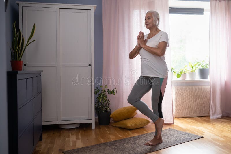 En mogen kvinna som står i trädet och som håller en balanserad träning arkivbilder
