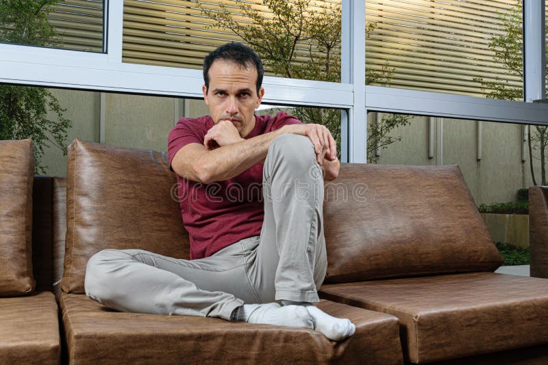 44-year-old man in a photo session on the brown sofa, doing various poses, joy, serious, sadness, with smartphone in hand and staring at the camera. 44-year-old man in a photo session on the brown sofa, doing various poses, joy, serious, sadness, with smartphone in hand and staring at the camera.