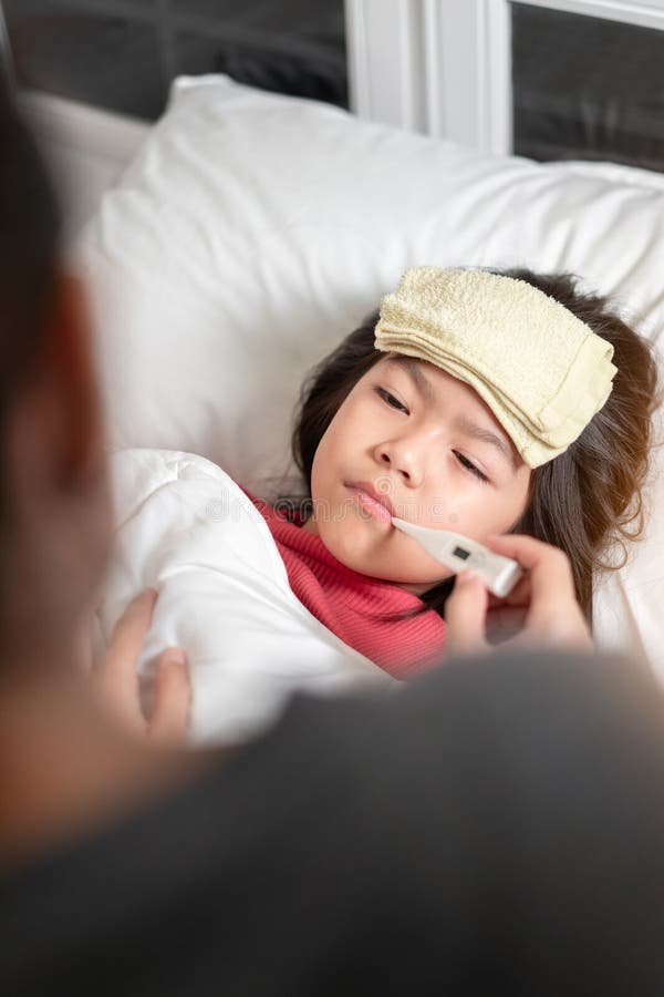 Asian mother measuring temperature girl with digital thermometer in her mouth on bed at morning time, Sick child have cool towel for reduce high fever, Selective focus, Healthy and infection concept. Asian mother measuring temperature girl with digital thermometer in her mouth on bed at morning time, Sick child have cool towel for reduce high fever, Selective focus, Healthy and infection concept.