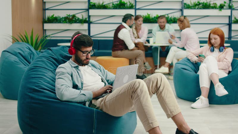 En mycket smart brunettman med skägg och glasögon arbetar seriöst på sin bärbara dator medan han lyssnar stock video