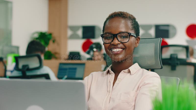 En mycket smart, svart kvinna med kort hår bär glasögon och en blus hon är på ett kontor och ser mycket bra ut stock video