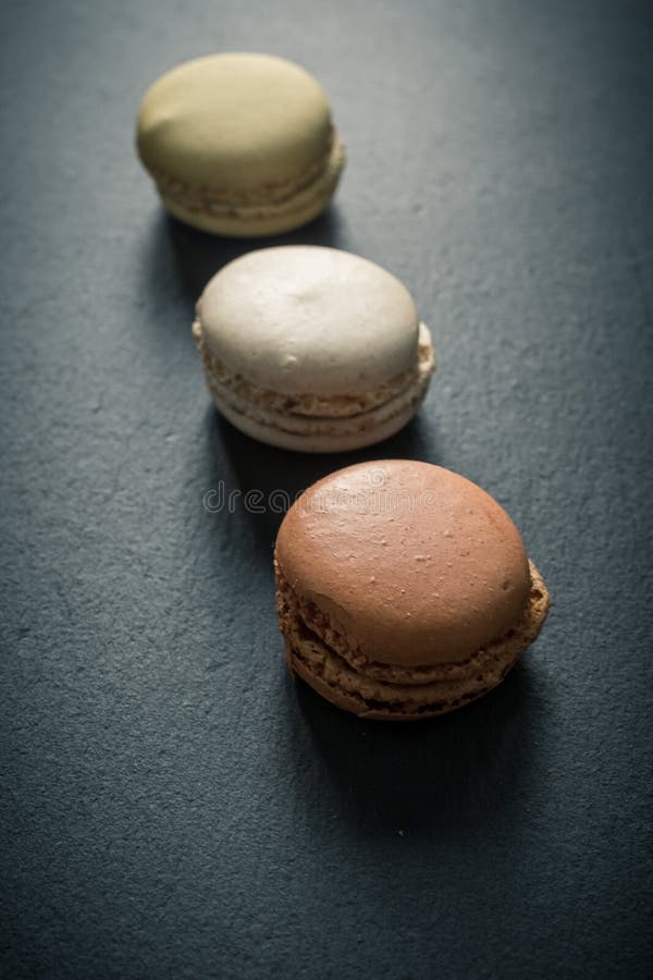 En mörk modig bild av chokladkaramel och vaniljmakaroner på en skifferbricka på en mörkgrå betongtextur royaltyfria foton