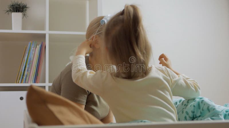 En omtänksam liten flicka som sitter på sängen placerar en medicinsk mask på mödrarnas ansikte stock video