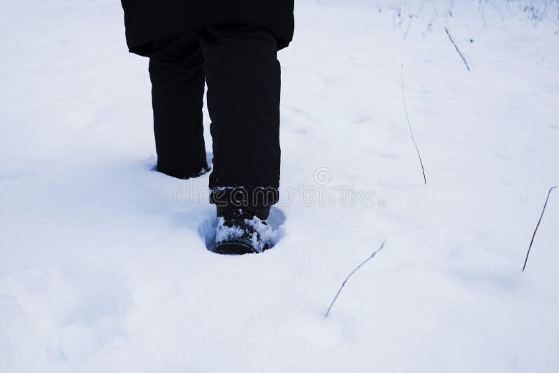 En person klädd i svarta byxor går genom snöregnet royaltyfria bilder