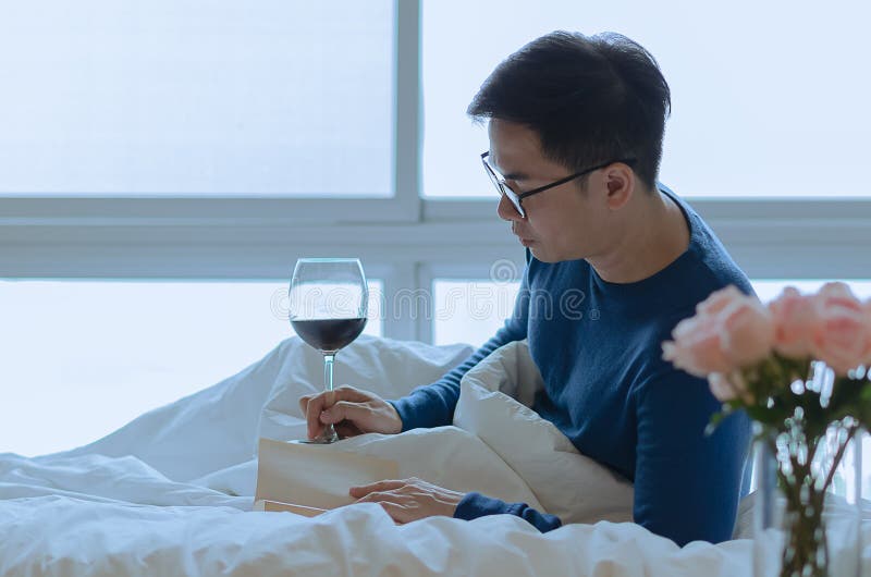 A person reading book on bed with a glass of red wine. Digital detox and social disconnect concept. A person reading book on bed with a glass of red wine. Digital detox and social disconnect concept