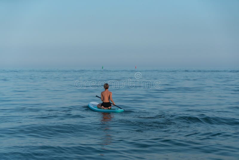 En pojke på 11 år som simmar på ett sup board i havet efter solnedgången. arkivfoto