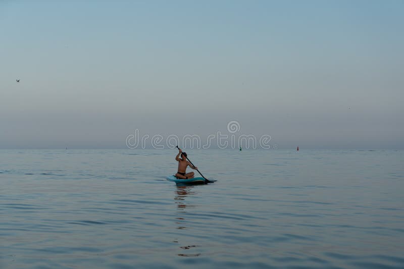 En pojke på 11 år som simmar på ett sup board i havet efter solnedgången. royaltyfri foto