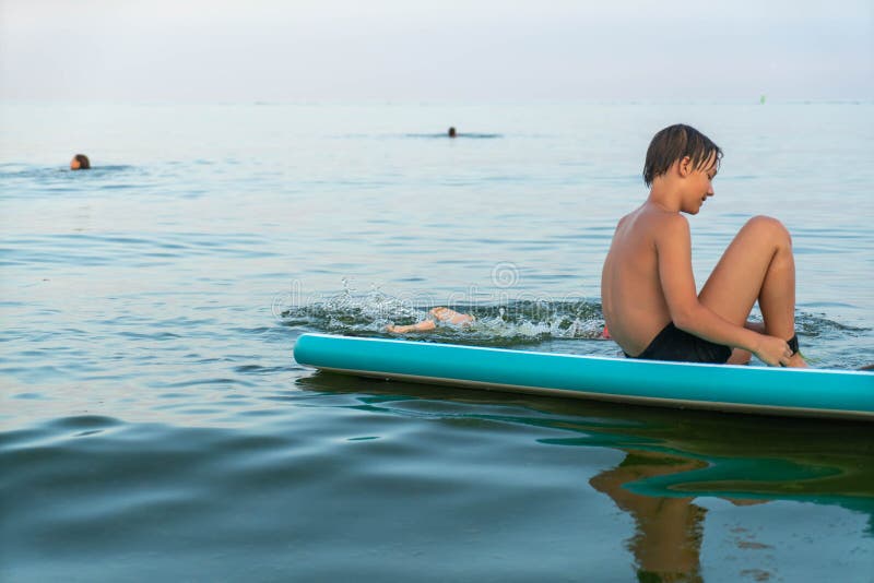 En pojke på 11 år som simmar på ett sup board i havet efter solnedgången. royaltyfria bilder