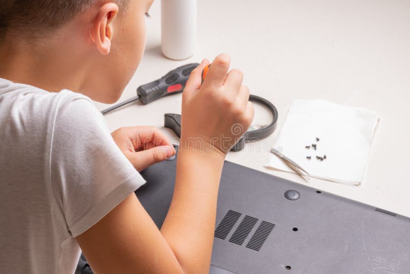 En pojke på 10 år sorterar en bärbar dator för rengöring och underhåll Selektivt fokus Screwdrivers, purge cylinder, förstoring royaltyfri foto