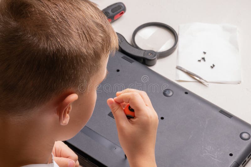 En pojke på 10 år sorterar en bärbar dator för rengöring och underhåll Selektivt fokus Screwdrivers, purge cylinder, förstoring royaltyfri foto