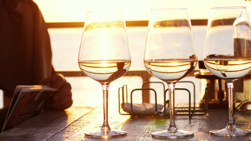 En romantisk matställe i sommar på en strand på solnedgången med tre exponeringsglas av vitt vin och en flaska av vinet vid havet arkivbild En romantisk matställe i sommar på en strand på solnedgången med tre exponeringsglas av vitt vin och en flaska av vinet vid havet arkivbild