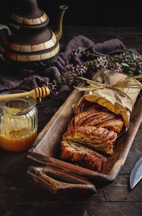 En rustik sammansättning av ett sött, slipat bakverk i en träbricka åtföljd av en honungsburk med en dipper med en vintagteapot oc royaltyfri fotografi
