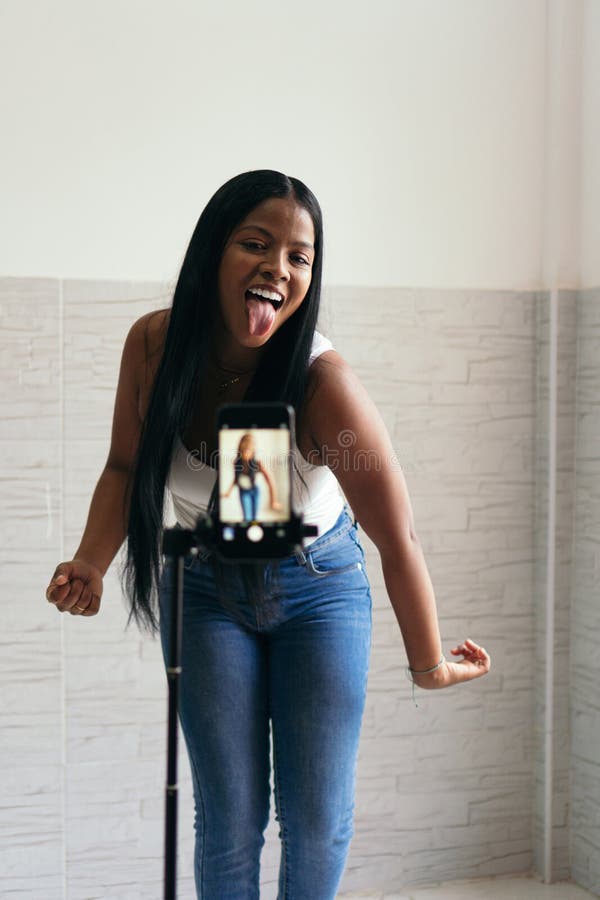 En självsäker kvinna som filmar sig hemma och dansar. hon använder mobiltelefon på stativ för att filma royaltyfri fotografi