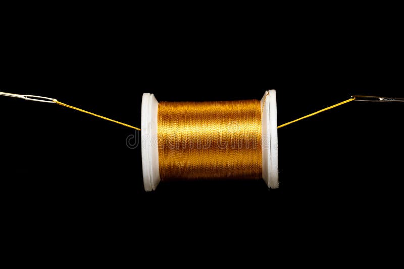 A spool of gold thread suspended on a field of black on a thread between 2 needle eyes.  Plenty of space for copy above and below the spool. A spool of gold thread suspended on a field of black on a thread between 2 needle eyes.  Plenty of space for copy above and below the spool