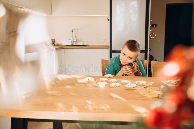 En skolpojke i köket dekorerar julkakor i soligt väder. Barn i köks hemmakonst fotografering för bildbyråer