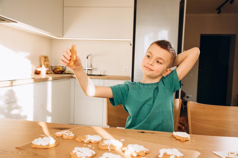 En skolpojke i köket dekorerar julkakor i soligt väder. Barn i köks hemmakonst arkivfoton