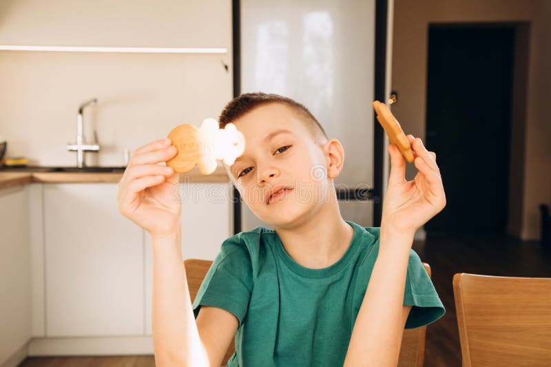 En skolpojke i köket dekorerar julkakor i soligt väder. Barn i köks hemmakonst arkivbild