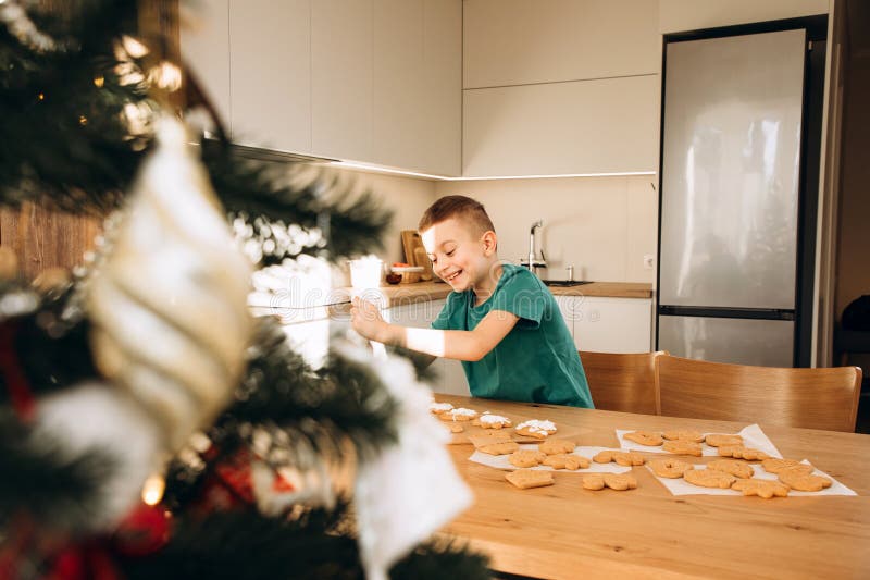 En skolpojke i köket dekorerar julkakor i soligt väder. Barn i köks hemmakonst arkivfoto