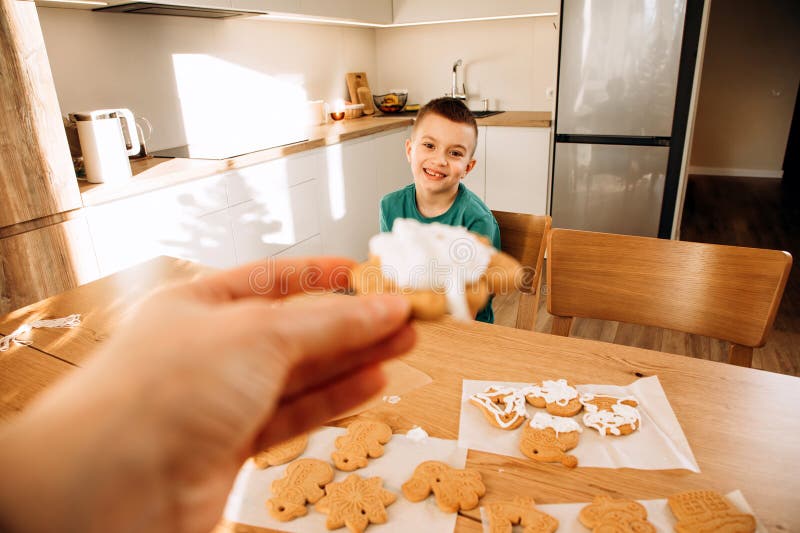 En skolpojke i köket dekorerar julkakor i soligt väder. Barn i köks hemmakonst royaltyfri foto