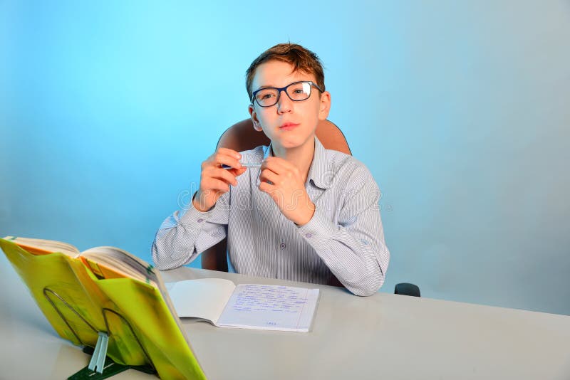 En smart student med exponeringsglas sitter på ett skolaskrivbord och gör läxa royaltyfria foton En smart student med exponeringsglas sitter på ett skolaskrivbord och gör läxa royaltyfria foton