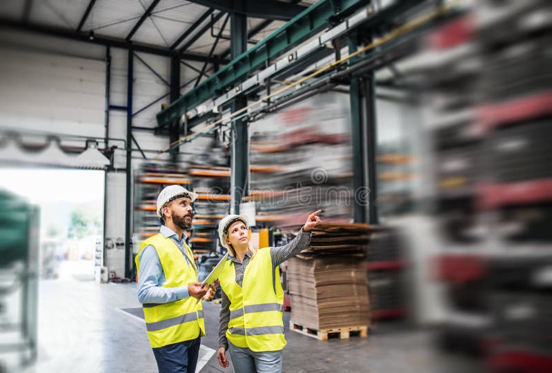En stående av en industriell man- och kvinnatekniker med minnestavlan i en fabrik som arbetar arkivfoton En stående av en industriell man- och kvinnatekniker med minnestavlan i en fabrik som arbetar arkivfoton