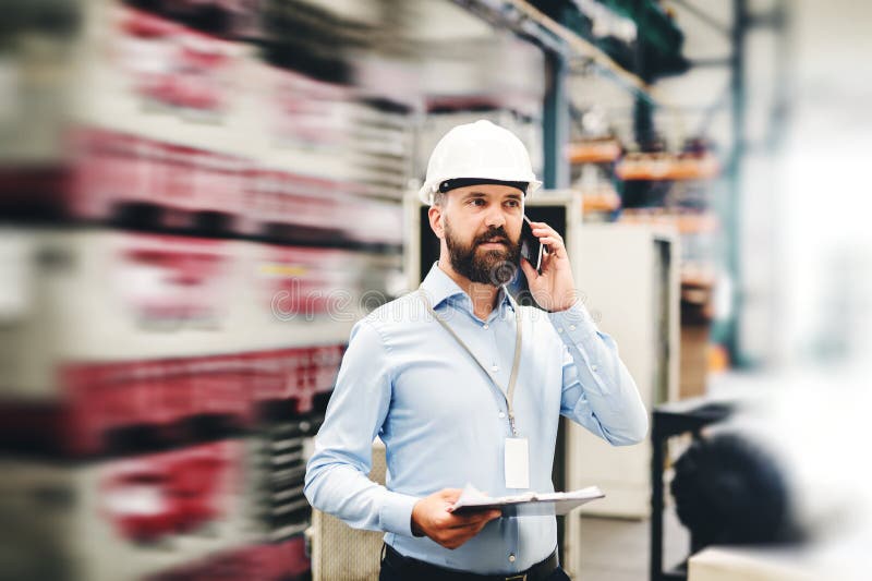 En stående av en industriell mantekniker med smartphonen i en fabrik som arbetar royaltyfri fotografi En stående av en industriell mantekniker med smartphonen i en fabrik som arbetar royaltyfri fotografi