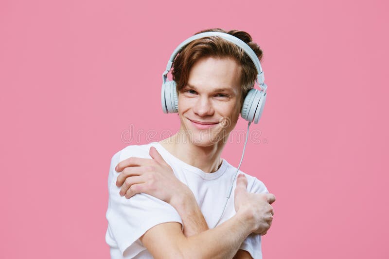 En söt snygg kille lyssnar på musik i hörlurarna som kramar sig med armarna runt axlarna. arkivbilder