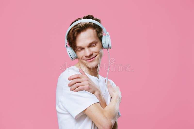 En söt snygg kille lyssnar på musik i hörlurarna som kramar sig med armarna runt axlarna. royaltyfri bild